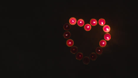 Draufsicht-Auf-Brennende-Rote-Kerzen-In-Form-Eines-Romantischen-Herzens,-Das-Auf-Schwarzem-Hintergrund-Ausgeblasen-Wird